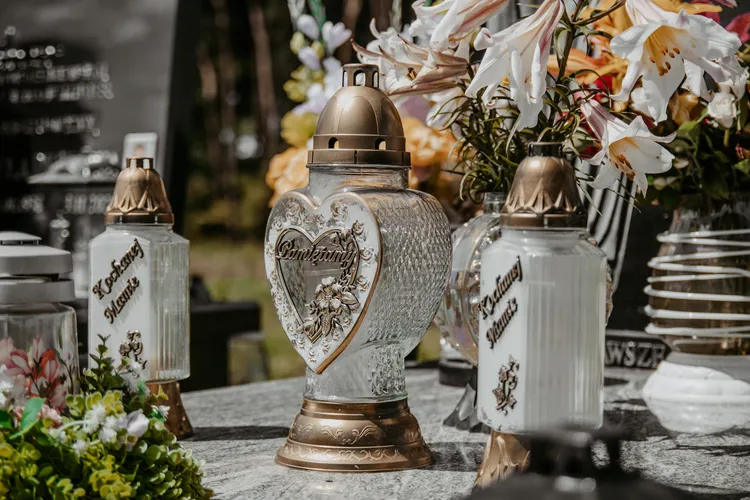 3 złote znicze stojące na grobie. Kwiaty w tle.